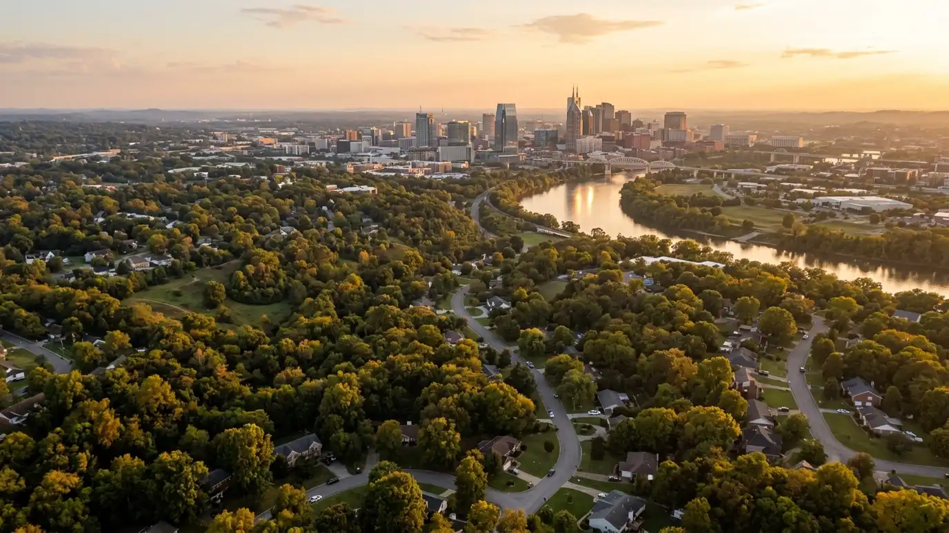 A golden sunset aerial view over a winding river, dense green suburban neighborhoods and a distant city skyline